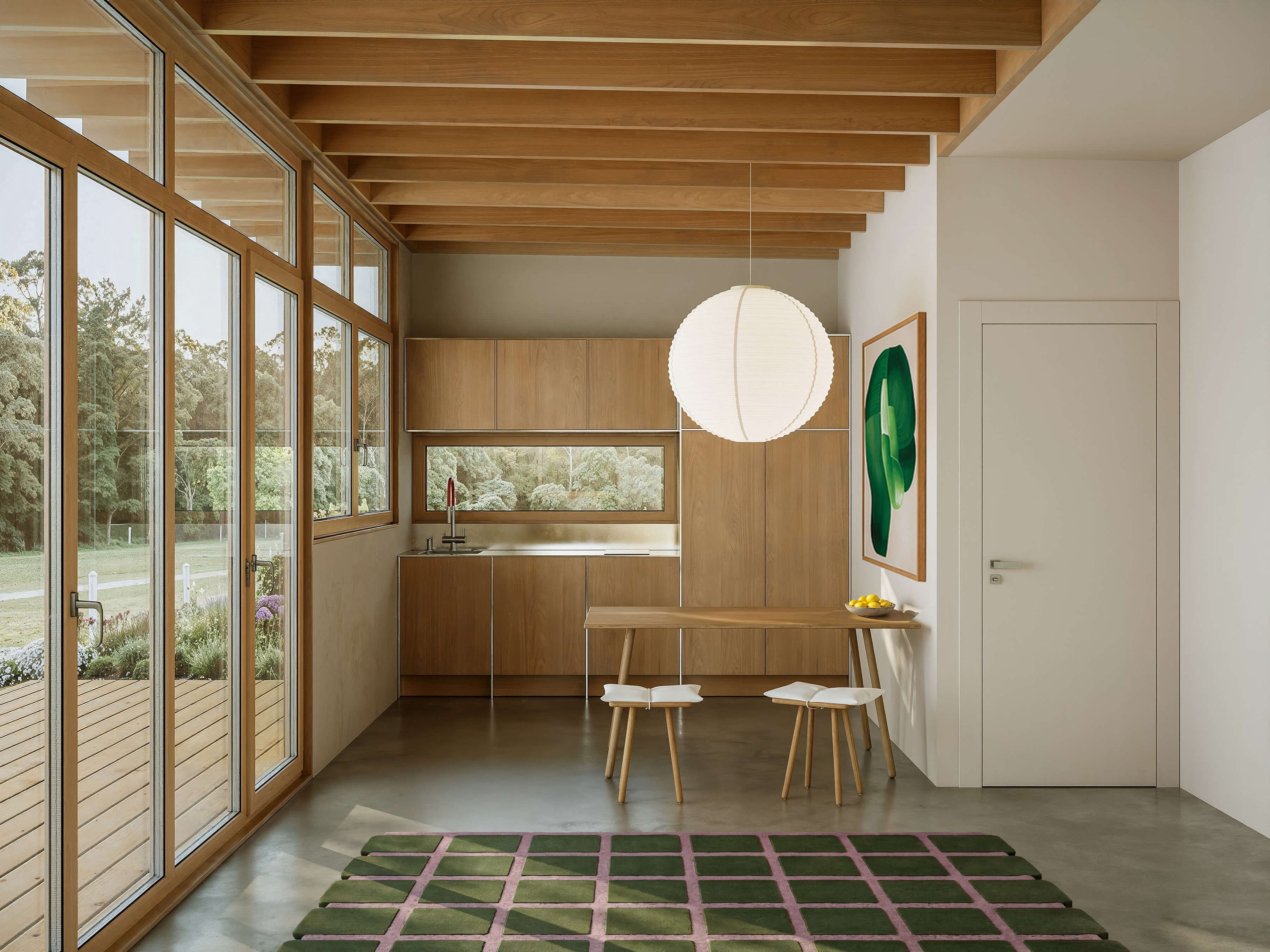 Modern kitchen with wooden cabinets, large windows, and a green rug on the floor.