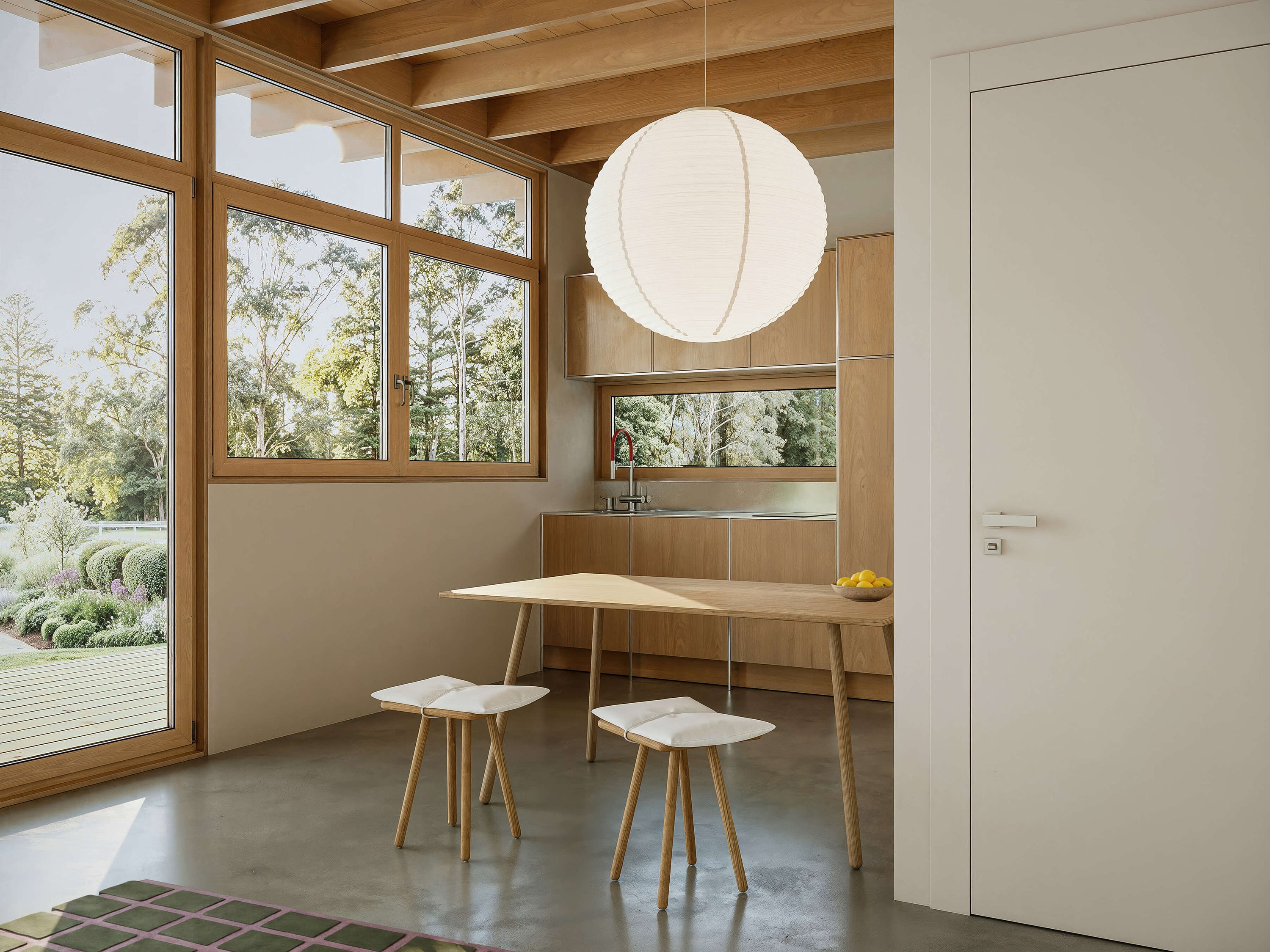 Modern interior with a dining area featuring a table and stools, large windows, and a light fixture.